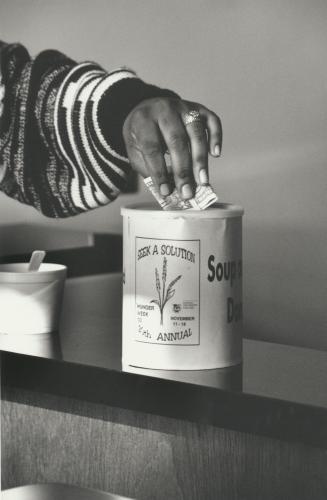 A hand placing a dollar bill into a can for Loyola Hunger Week.