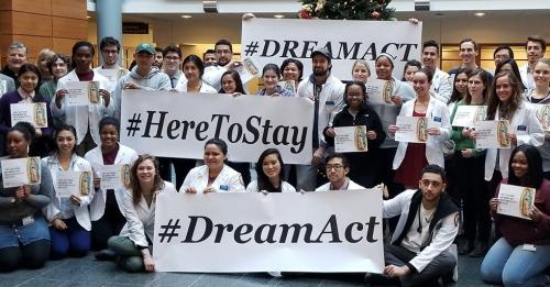 A large group of Loyola University Chicago medical students pose for the camera with signs and banners promoting the Dream Act. The banners read "#Dream Act and #Here To Stay."