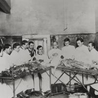 Ten students and a professor pose behind two operating tables in the Bennett Medical College Anatomy Lab. 